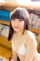 A woman in a white bra sitting on the floor in front of a bookshelf.