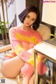 A woman in a pink and yellow sweater sitting on a chair.