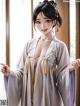 A woman in a white kimono standing in front of a window.