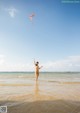 A naked woman flying a kite on the beach.