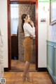 A woman in a white shirt and brown skirt standing in a hallway.